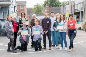 A group of people are standing together. Some are kneeling. Some of the people are holding certificates. They are smiling.